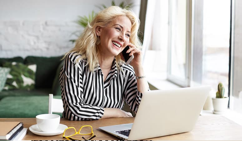 An elderly businesswoman in a striped blouse making a phone call to a potential client