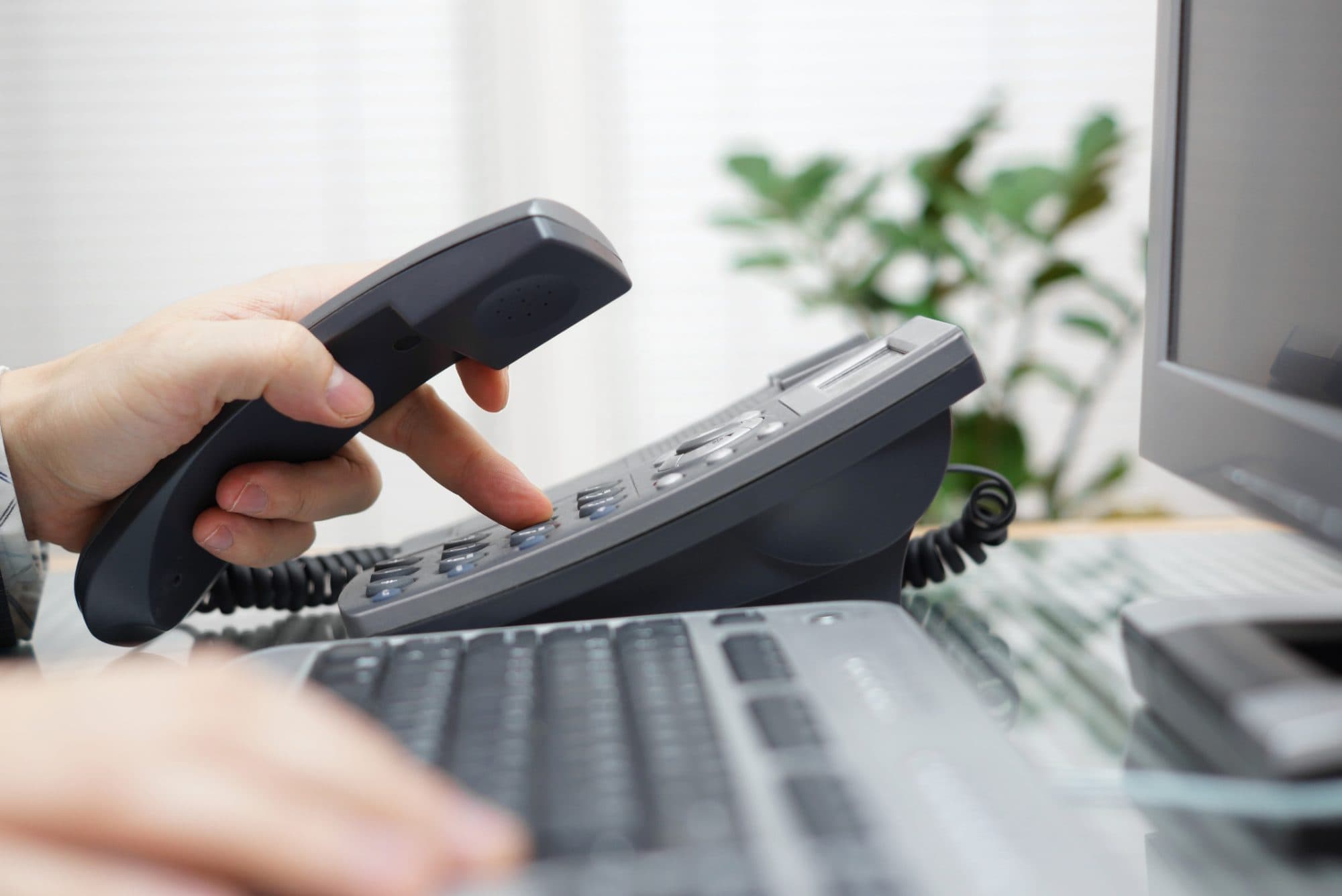 Person holding a phone handset and pressing a key on an office desk phone
