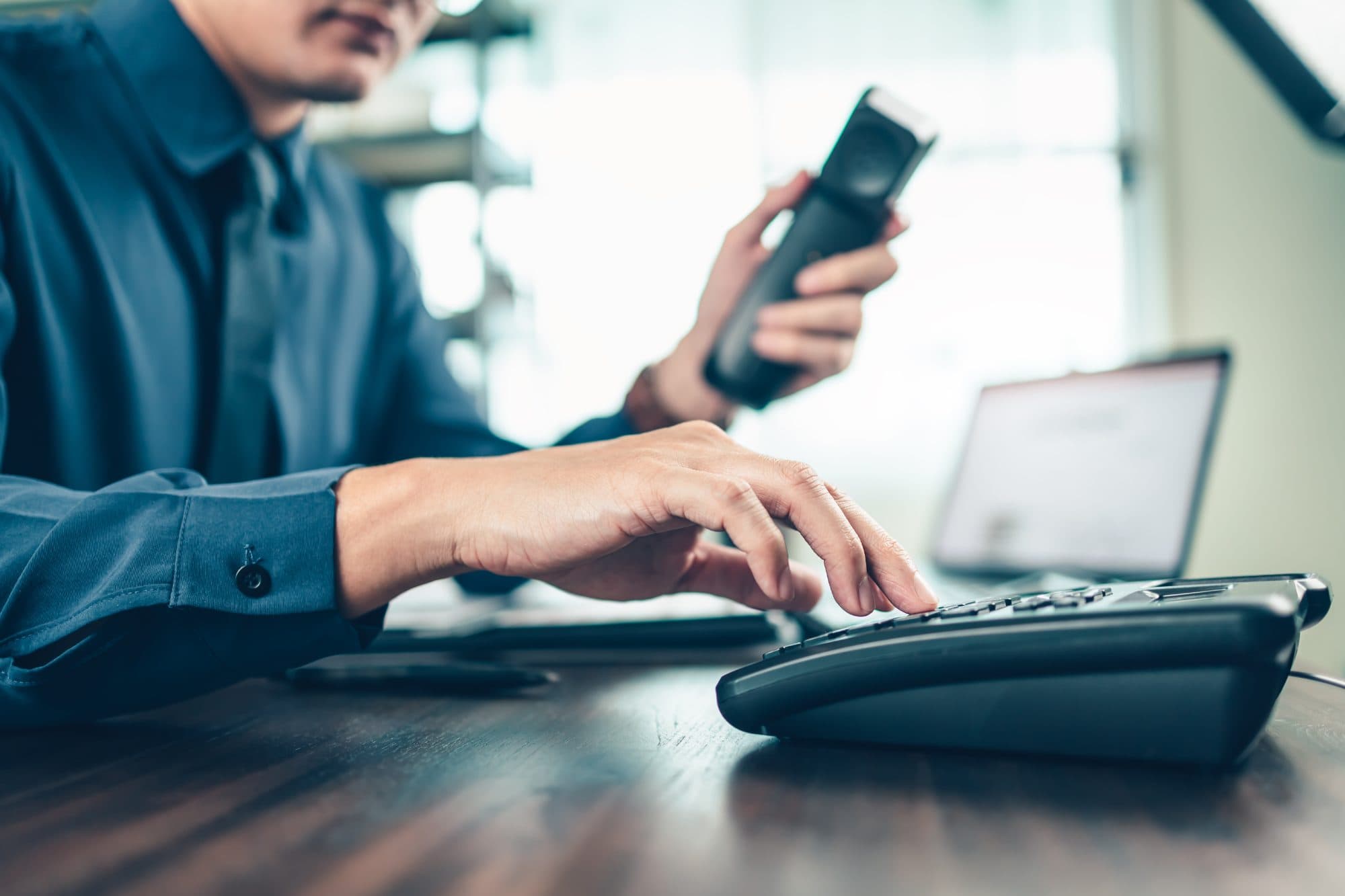 Man holding a phone handset and pressing keys on a desk phone keypad